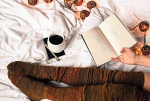 donna con calzettoni che legge un libro sul letto con luci soffuse in stile hygge