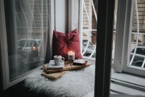 angolo di relax vicino alla finestra con coperte, cuscino e candele. In pieno stile hygge
